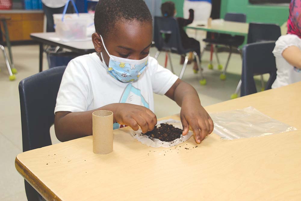 NCES PreK student Semaj Clemons completes the final steps of planting his seed. Becky Monk is the NCES PreK teacher and Paula Berryhill is the NCES Science Lab Instructor.