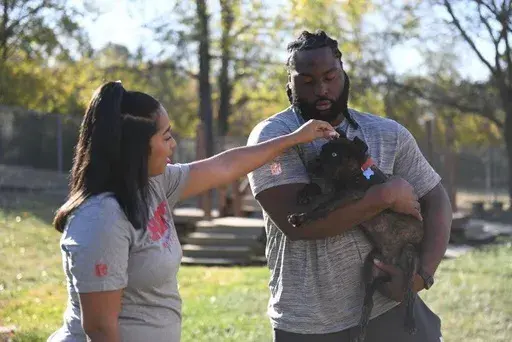 Kansas City Chiefs defensive tackle Derrick Nnadi, right, and his girlfriend Nani Hinton, left, pets Parsnip, a puppy from The Humane Society of Greater Kansas City that was featured in the Puppy Bowl XXI, Monday, Oct. 21, 2024, in Kansas City, Kan. (AP Photo/Nick Ingram)