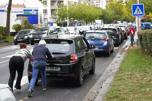 People push their car in a line of vehicles waiting to reach a station, Friday, Oct. 14, 2022 in Nanterre, outside Paris. Strikes in the French refineries of TotalEnergies group were still going on Friday, heavily disrupting fuel supplies as hard-left CGT union rejected a deal over pay rise that has been found between the energy giant and two other more moderate unions. (AP Photo/Michel Euler)