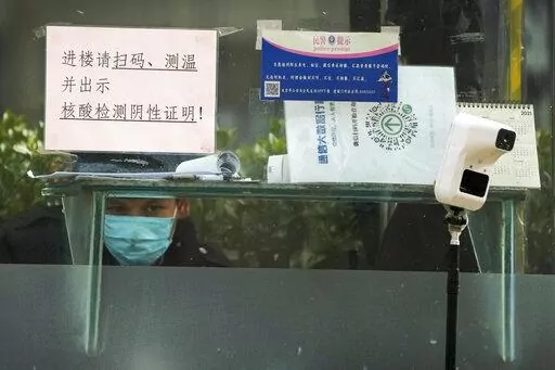 A security guard keeps watch inside a booth displaying a temperature scan device and a travel QR code, outside an office building in Beijing, Monday, Dec. 12, 2022. China will drop a travel tracing requirement as part of an uncertain exit from its strict "zero-COVID" policies that have elicited widespread dissatisfaction. (AP Photo/Andy Wong)