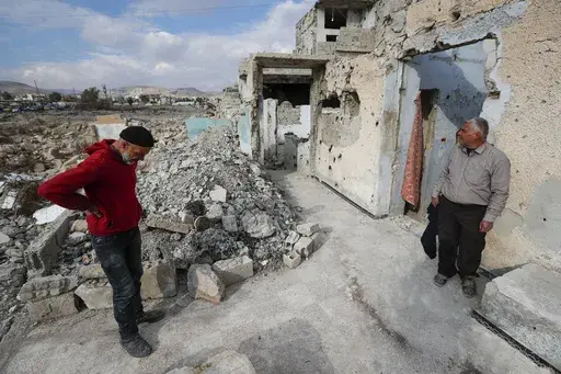 Samir al-Baghdadi, 46, left, stands on his brother Fayez outside his family's home that was destroyed during the civil war in the Qaboun neighborhood of Damascus, Syria, Saturday, Jan. 11, 2025. (AP Photo/Omar Sanadiki)