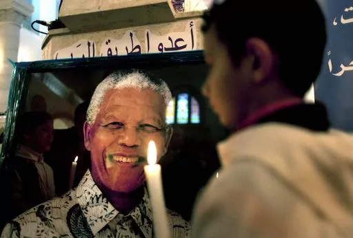 FILE — A Palestinian child holds a lit candle as he prays in front of a poster of late South African leader Nelson Mandela, during a special service in his honor at the Holy Family Church, in the West Bank city of Ramallah, Sunday, Dec. 8, 2013. South Africa's long-held support for the Palestinian people can be traced back to the time of the late Nelson Mandela and Palestinian leader Yasser Arafat, with the two leaders believing that the struggle for freedom by Blacks in apartheid South Africa