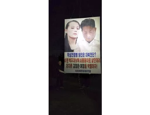 In this photo provided by Fighters for a Free North Korea, Park Sang-hak holds a placard carrying pictures of North Korean leader Kim Jong Un and his sister Kim Yo Jong in Ganghwa, South Korea Sunday, Sept. 4, 2022. Park said he has again flown huge balloons carrying COVID-19 relief items and an anti-North Korea placard across the tense inter-Korean border, despite the North’s recent warning of a deadly attack over his activities. A part of letters read "Let's eradicate Kim Jong Un and (his si