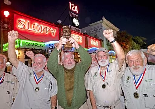In this Saturday, July 22, 2023, photo provided by the Florida Keys News Bureau, Gerrit Marshall, center, hoists his trophy after winning the Hemingway Look-Alike Contest at Sloppy Joe's Bar in Key West, Fla. After 11 years of competing Marshall, a Madison, Wisc., resident, finally achieved success on his 68th birthday. Flanking Marshall, from left, are previous winners including Tom Grizzard, Wally Collins and John Stubbings. The competition was a highlight of the annual Hemingway Days festival