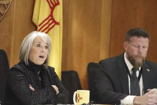 New Mexico Gov. Michelle Lujan Grisham, left, and Senior Public Safety Advisor Ben Baker, right, provide an update, Monday, Dec. 11, 2023, in Santa Fe, New Mexico, on a public health order aimed at reining in gun violence and drugs in the Albuquerque area that the governor describes as an epidemic. New Mexico could become an early political testing ground for a proposal to make assault-style weapons less deadly. (AP Photo/Morgan Lee)