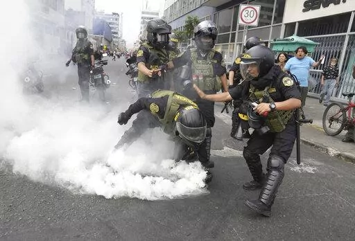 Police officers pick up a tear gas canister that was thrown back at them by anti-government protesters who traveled to the capital from across the country to march against Peruvian President Dina Boluarte in Lima, Peru, Wednesday, Jan. 18, 2023. Protesters are seeking immediate elections, Boluarte's resignation, the release of ousted President Pedro Castillo and justice for the dozens of protesters killed in clashes with police. (AP Photo/Martin Mejia)
