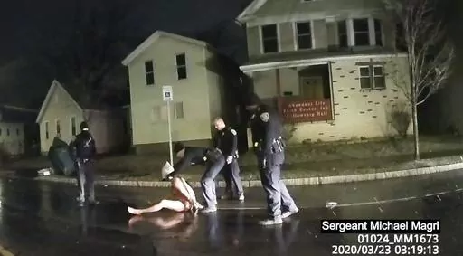 FILE- This image from police body camera video provided by Roth and Roth LLP, shows a Rochester police officer as he puts a hood over the head of Daniel Prude in Rochester, N.Y., March 23, 2020. Prude died after police held him down until he stopped breathing after encountering him running naked through the snowy streets of Rochester, NY. On Thursday, Oct. 12, 2023, a leading doctors group has formally withdrawn its approval of a 2009 paper on “excited delirium,” a document that critics say 