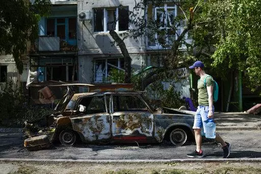 A man carries water in front of an apartment building damaged in an overnight missile strike, in Sloviansk, Ukraine, Tuesday, May 31, 2022. In towns and cities near the fighting in eastern Ukraine, artillery and missile strikes have downed power lines and punched through water pipes, leaving many without electricity or water as repair crews race to repair the damage. (AP Photo/Francisco Seco)