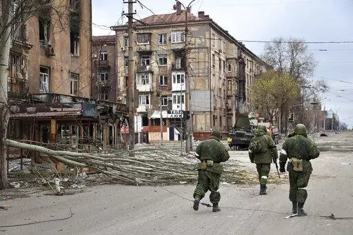 Servicemen of the militia from the Donetsk People's Republic walk past damaged apartment buildings near the Illich Iron & Steel Works Metallurgical Plant, the second-largest metallurgical enterprise in Ukraine, in an area controlled by Russian-backed separatist forces in Mariupol, Ukraine, Saturday, April 16, 2022. Mariupol, which is part of the industrial region in eastern Ukraine known as the Donbas, has been a key objective for Russia since the start of the Feb. 24 invasion. (AP Photo/Alexei 