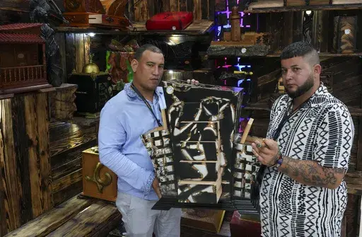 Artisans Adrian Moran, left, and Ariel Sanchez, the creators of Clave Humidors, pose with one o their cigar humidifiers during the XXV Cigar Festival at Convention Palace in Havana, Monday, Feb. 24, 2025. (AP Photo/Ramon Espinosa)
