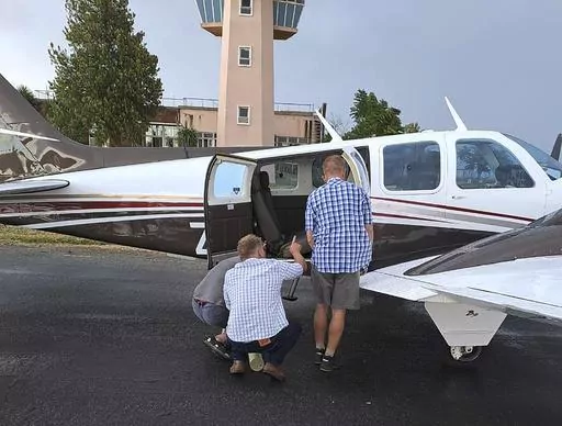 In this photo provided by Brian Emmenis, people look inside a plane at the Welkom Airport, in Welkom, South Africa, as they search for a venomous snake that the pilot found hiding under his seat midair, Monday April 3, 2023. Rudolf Erasmus had four passengers on board the light aircraft during Monday's flight when he felt “something cold” slide across his lower back. He glanced down to see the head of a fairly large Cape Cobra “receding back under the seat,” he said. (Brian Emmenis via A