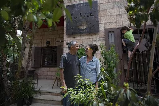 Kenae Totah, 5, right, plays while his parents Morgan Cooper, 41, center and Saleh Totah, right, pose for a photo in front of their restaurant, at the West Bank city of Ramallah, Monday, May 2, 2022.  The Israeli military body in charge of civilian affairs in the occupied West Bank has developed a new policy that would heavily regulate entry into the territory. Critics say it extends Israel's nearly 55-year military rule even further into every corner of Palestinian society. It would impose new 