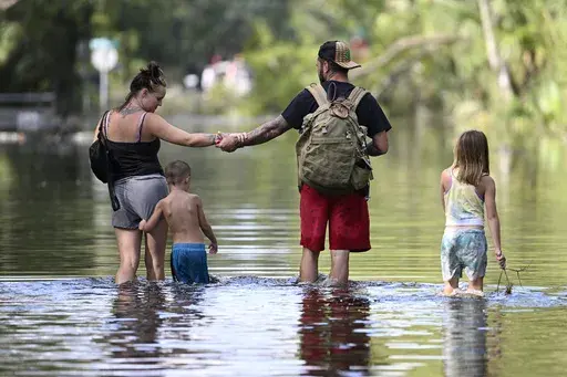 Dustin Holmes, second from right, holds hands with his girlfriend, Hailey Morgan, while returning to their flooded home with her children Aria Skye Hall, 7, right, and Kyle Ross, 4, in the aftermath of Hurricane Helene, Sept. 27, 2024, in Crystal River, Fla. (AP Photo/Phelan M. Ebenhack, File)