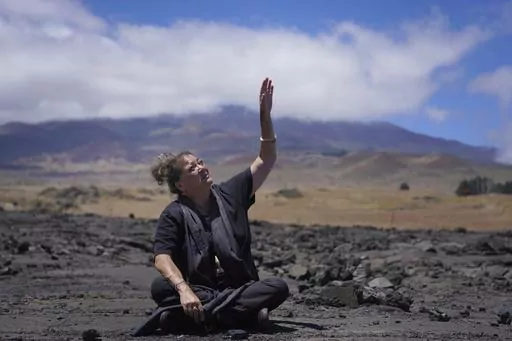 Kealoha Pisciotta, a cultural practitioner and longtime activist, sits on lava rock part of the way up Mauna Kea while giving an interview on the Big Island of Hawaii, on Saturday, July 15, 2023. Over the last 50 years, astronomers have mounted 13 giant astronomical observatories on Mauna Kea's summit. In 2019, Native Hawaiians including Piscioitta staged a year-long protest over construction of an additional telescope. (AP Photo/Jessie Wardarski)