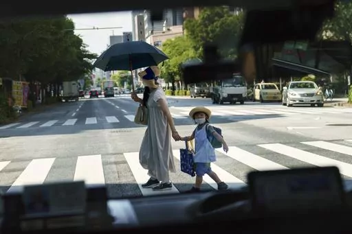 A pedestrian crossing a street with a child is seen through a taxi window in Tokyo, Monday, July 19, 2021. The number of babies born in Japan last year fell for an eighth straight year to a new low, government data showed Tuesday, Feb. 27, 2024, and a top official said it was critical for the country to reverse the trend in the coming half-dozen years. (AP Photo/David Goldman, File)