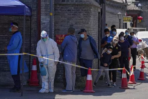 A worker in protective suit sprays disinfectant as residents line up for mass COVID test on Monday, May 16, 2022, in Beijing. Authorities say most of Shanghai has stopped the spread of the coronavirus in the community and fewer than 1 million people remain under strict lockdown. China's largest city is moving toward reopening as economic data showed the gloomy impact of China's "zero-COVID" policy. (AP Photo/Andy Wong)