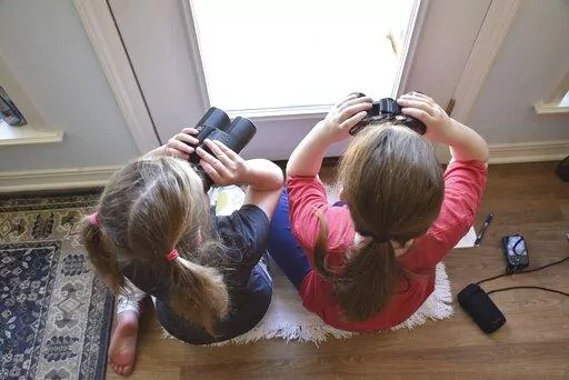 This image provided by Macaulay Library/Cornell Lab of Ornithology shows two girls watching birds through a window with binoculars, bird lists and cameras in Elm Grove, Louisiana, during the Great Backyard Bird Count in February 2022. About 385,000 people from 192 countries took part in the 2022 count, and their results have been used by scientists to study bird populations worldwide. (Emily Tubbs/Macaulay Library/Cornell Lab of Ornithology via AP)