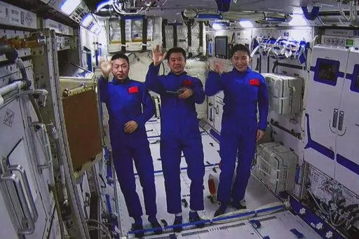 In this photo released by Xinhua News Agency, an image taken off the screen at the Beijing Aerospace Control Center shows Chinese astronauts from left, Cai Xuzhe, Chen Dong and Liu Yang wave from inside the Wentian lab module on Monday, July 25, 2022. China added the laboratory to its permanent orbiting space station Monday as it moves toward completing the structure in coming months. (Guo Zhongzheng/Xinhua via AP)