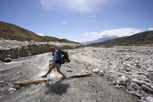 Lauren Lamberts, of Belgium, crosses water flowing over a section of the Pacific Crest Trail washed away by storms while trail repairs have been disrupted by federal cuts Thursday, April 3, 2025, near Whitewater, Calif. (AP Photo/Gregory Bull)