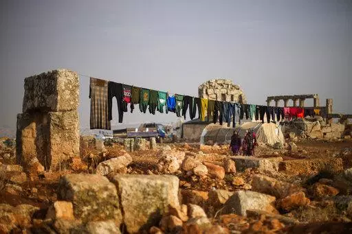 Syrian displaced people walk next to ancient Roman era ruins where they have set their tends in Sarmada district, north of Idlib city, Syria, Thursday, Nov. 25, 2021.  Fallout from the 2-month-old war in Ukraine is worsening long-term humanitarian crises elsewhere, including in Syria.  (AP Photo/Francisco Seco, File)