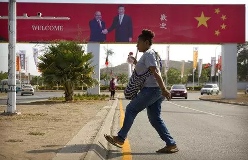 A woman crosses the street near a billboard commemorating the state visit of Chinese President Xi Jinping in Port Moresby, Papua New Guinea, Nov. 15, 2018. China wants 10 small Pacific nations to endorse a sweeping agreement covering everything from security to fisheries in what one leader warns is a “game-changing” bid by Beijing to wrest control of the region. (AP Photo/Mark Schiefelbein, File)