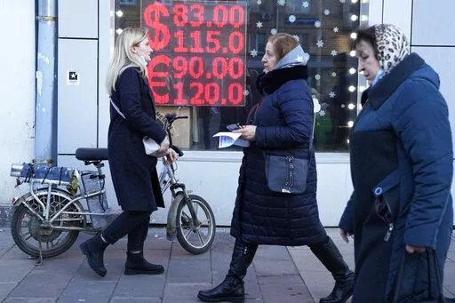 People walk past a currency exchange office screen displaying the exchange rates of U.S. Dollar and Euro to Russian Rubles in Moscow's downtown, Russia, Feb. 28, 2022. In the days since the West imposed sanctions on Russia over its invasion of Ukraine, ordinary Russians are feeling the painful effects — from payment systems that won't operate and problems withdrawing cash to not being able to purchase certain items. (AP Photo/Pavel Golovkin, File)