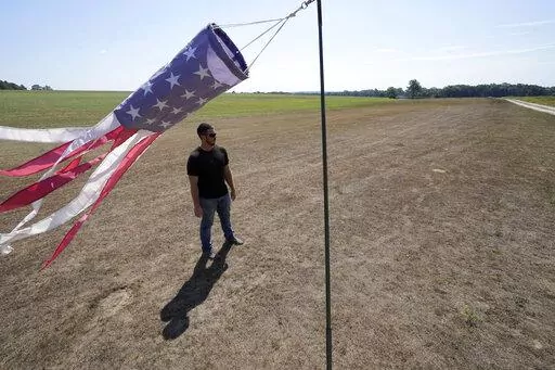 Hay farmer Milan Adams stands in a dry hay field near a wind sock, left, in Exeter, R.I., Tuesday, Aug. 9, 2022. Adams said in prior years it rained in the spring. This year, he said, the dryness started in March, and April was so dry he was nervous about his first cut of hay. (AP Photo/Steven Senne)