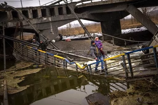 Local militiaman Valery, 37, carries a child as he helps a fleeing family across a bridge destroyed by artillery, on the outskirts of Kyiv, Ukraine, Wednesday, March 2. 2022.  Russian forces have escalated their attacks on crowded cities in what Ukraine's leader called a blatant campaign of terror. (AP Photo/Emilio Morenatti)