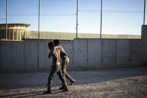 A migrant helps another as they arrive on Spanish soil after crossing the fences separating the Spanish enclave of Melilla from Morocco, in Melilla, Spain, Thursday March 3, 2022. Hundreds of Africans have tried to climb over the fences separating the Spanish city of Melilla from Morocco for the second consecutive day and the Spanish government's delegation in Melilla says that 380 of 1,200 migrants who had attempted to cross managed to overcome the double 6-meter (20-feet) barrier that perimete