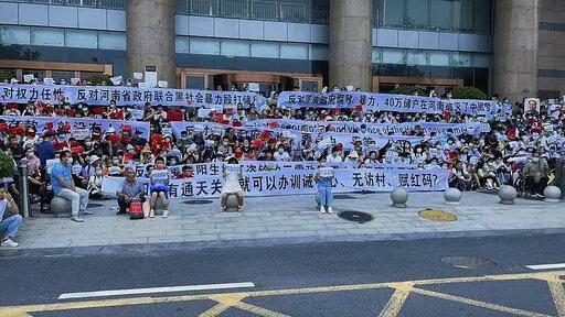 In this photo released by Yang on Sunday, July 10, 2022, people hold banners and chant slogans during a protest at the entrance to a branch of China's central bank in Zhengzhou in central China's Henan Province. A large crowd of angry Chinese bank depositors faced off with police Sunday, some reportedly injured as they were roughly taken away, in a case that has drawn attention because of earlier attempts to use a COVID-19 tracking app to prevent them from mobilising. (AP Photo/Yang)