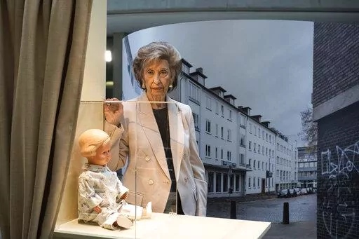 Holocaust survivor Lore Mayerfeld poses next to her doll 'Inge' as part of an exhibition with items from Israel's Yad Vashem Holocaust memorial in the German parliament Bundestag in Berlin, Germany, Monday, Jan. 23, 2023. An exhibition marking the 70th anniversary of Israel's Yad Vashem Holocaust memorial brings back to Germany a diverse set of everyday objects that Jews took with them when they fled the Nazis. (AP Photo/Markus Schreiber)