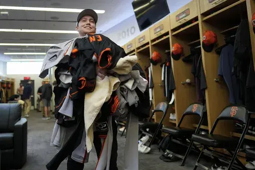San Francisco Giants clubhouse attendant Riley Halpin gathers a mound of dirty clothes in the clubhouse after spring training baseball practice at the team's facility, Monday, Feb. 17, 2025, in Scottsdale, Ariz. (AP Photo/Carolyn Kaster)