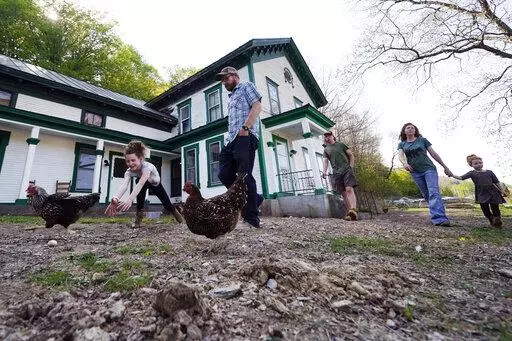 Soraya Holden, left, chases a chicken while walking with her family past their family home, Thursday, May 12, 2022, in Proctor, Vt. After fleeing one of the most destructive fires in California, the Holden family wanted to find a place that had not been so severely affected by climate change and chose Vermont. (AP Photo/Charles Krupa)