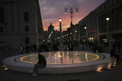 Locals and tourists walk along a main street near St. Peter's Basilica, background, as the sun sets in Rome, Italy, Friday, March 7, 2025. (AP Photo/Francisco Seco)