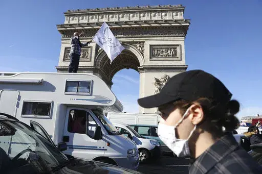 A protester stands atop a camper van as a convoy drives past the Arc de Triomphe on the Champs-Elysees avenue, Saturday, Feb.12, 2022 in Paris, in protests against virus restrictions inspired by the Canada's horn-honking "Freedom Convoy." On Friday, Feb. 18, 2022, The Associated Press reported on stories circulating online incorrectly asserting that Parisian police ticketed protesters for carrying the French flag and saying the word “freedom.” But tickets were given to protesters for offense