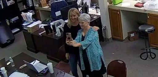 In this Jan. 7, 2021, image taken from Coffee County, Ga., security video, Cathy Latham, right, appears to take a selfie with a member of a computer forensics team inside the local elections office. Lawyers for three Georgia Republicans, including Latham, who falsely claimed that Donald Trump won the state and they were “duly elected and qualified” electors, are set to argue that their criminal charges should be moved from state to federal court(Coffee County, Georgia via AP)