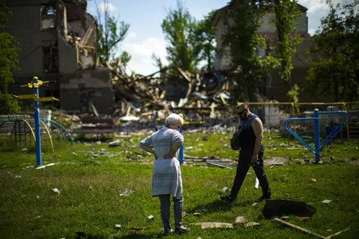 Local residents stand next to a school destroyed in a Russian bombing in Bakhmut, eastern Ukraine, Tuesday, May 24, 2022. The town of Bakhmut has been coming under increasing artillery strikes, particularly over the last week, as Russian forces try to press forward to encircle the city of Sieverodonetsk to the northeast. (AP Photo/Francisco Seco)