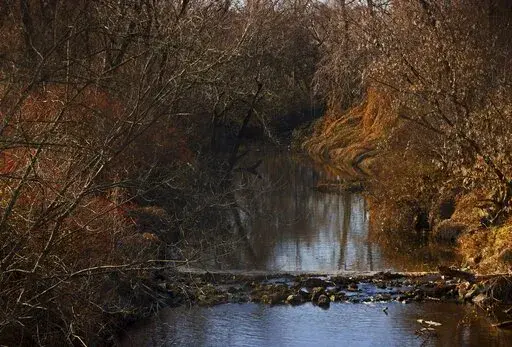 Water flows in Coldwater Creek on Thursday, Dec. 9, 2021, behind a row of homes at Belcroft Drive and Old Halls Ferry Road in Missouri's St. Louis County. Environmental investigation consultants have found significant radioactive contamination at an elementary school, which sits in the flood plain of Coldwater Creek which was contaminated by nuclear waste from weapons production during World War II. (Christian Gooden/St. Louis Post-Dispatch via AP)