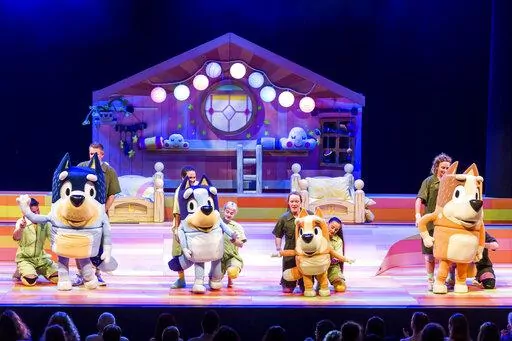 This image shows characters, from left, Bandit, Bluey,  Bingo and Chili and their puppeteers during a performance of “Bluey’s Big Play." The theatrical adaptation of the popular animated children’s TV show “Bluey” starts a multistate tour this month. (Darren Thomas via AP)