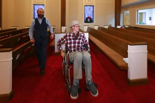 Jerry Lamb, who has a spine condition, talks to Pastor Adam Kelchner at Camden First United Methodist Church Thursday, Dec. 8, 2022, in Camden, Tenn. The church at the urging of the pastor recently had a couple pews cut in half so Jerry, and anyone else who uses a wheelchair, walker or other aid, can still sit with the rest of the congregation. (AP Photo/John Amis)
