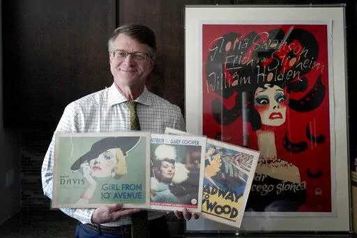 Dwight Cleveland, a major collector of movie posters and lobby cards, poses for a portrait with a three lobby card and movie poster Tuesday, Sept. 27, 2022, in Chicago. Many silent films from the early 1900s no longer exist. But they live on in movie theater lobby cards. More than 10,000 of the mostly 11-by-14-inch cards that promoted the cinematic romances, comedies and adventures of the era are being digitized for preservation and publication online, thanks to an agreement formed between a Chi